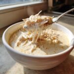 A spoonful of steaming homemade cream of chicken soup showing long strings of melted cheese and shredded chicken.
