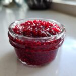Close-up of a small glass jar filled with vibrant, chunky homemade raspberry jam.