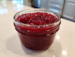 Close-up of a small glass jar filled with bright, chunky homemade raspberry jam.