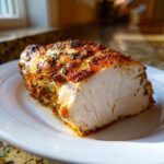 Cross-section of a perfectly cooked, juicy greek chicken breast showing white meat and a seasoned, herbed crust.
