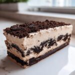 A thick slice of layered Oreo dirt cake showing dark cookie crumbs, light cream filling, and a cookie topping.