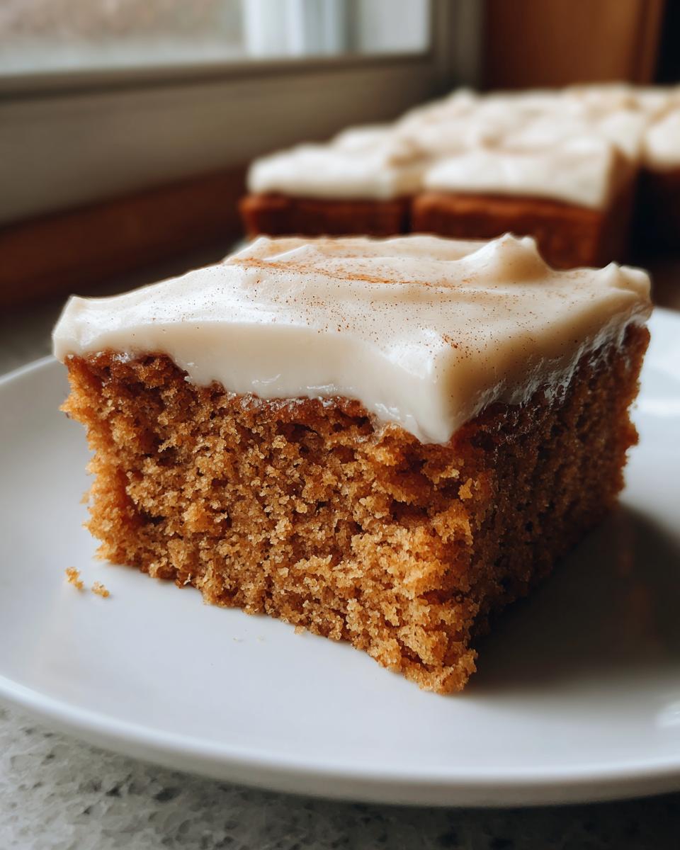 Close-up of a moist slice of applesauce cake topped with thick cream cheese frosting and a dusting of cinnamon.