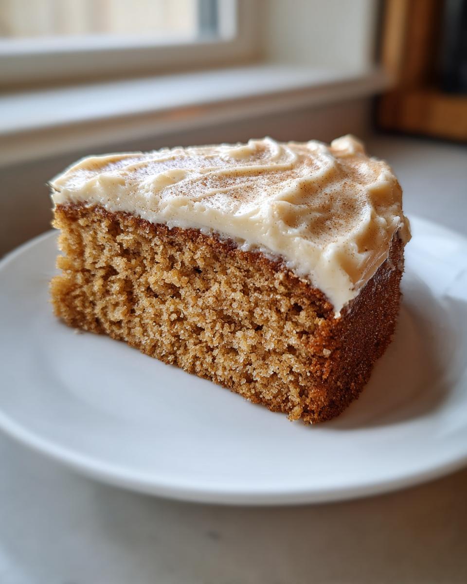 Close-up of a moist slice of applesauce cake topped with thick cream cheese frosting and a dusting of cinnamon.