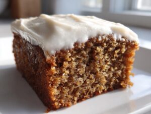 Close-up of a moist, rich brown slice of applesauce cake topped with thick white frosting.