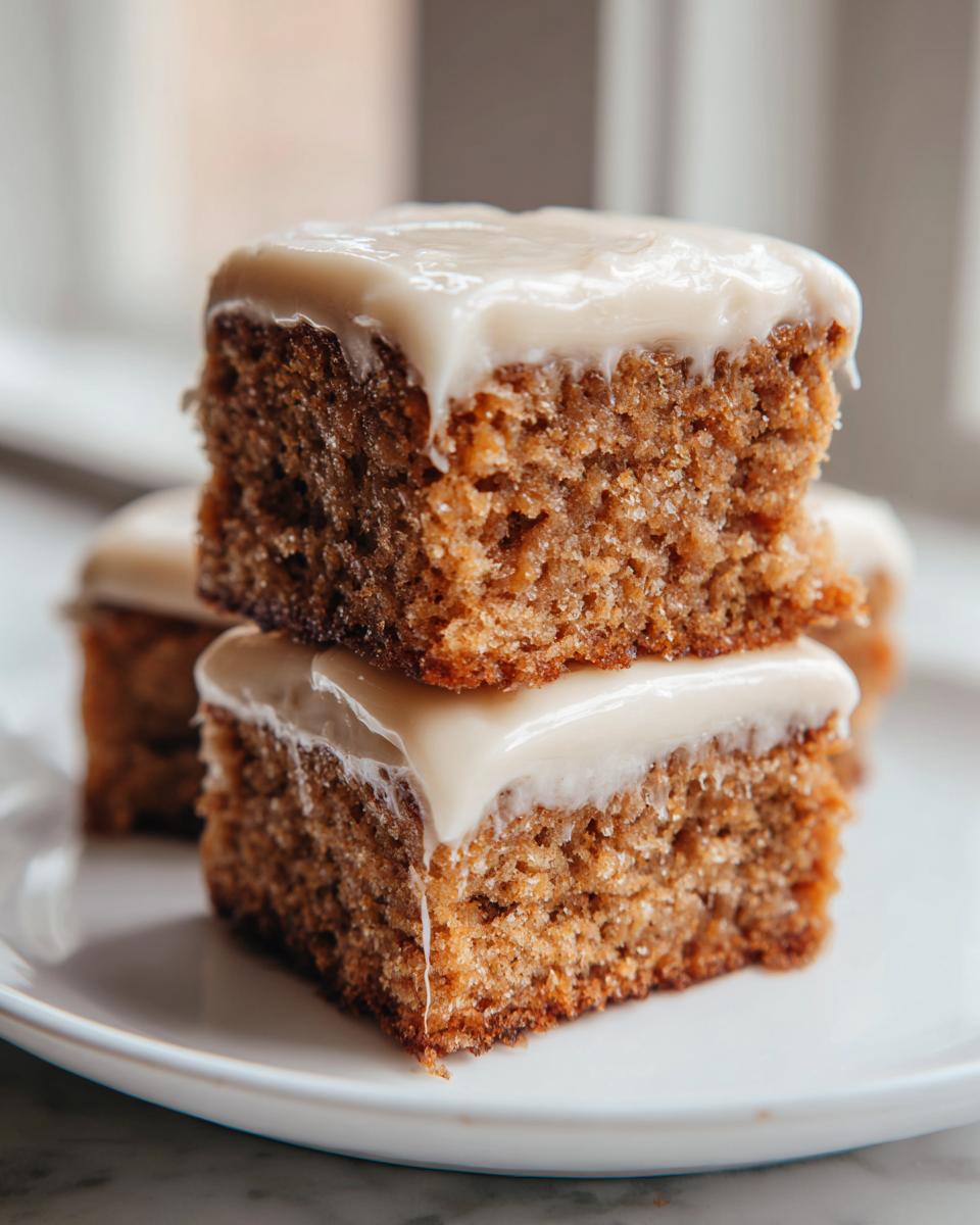 Two stacked squares of moist applesauce cake topped with thick, creamy white frosting.