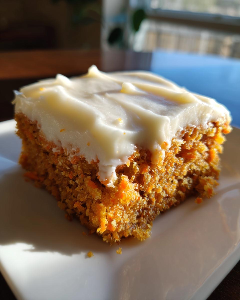 A close-up of a single square of moist carrot cake bars topped with thick cream cheese frosting.