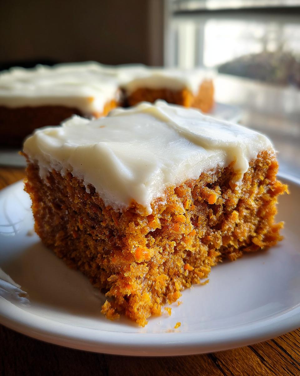 A close-up of a square slice of moist carrot cake bars topped with thick cream cheese frosting on a white plate.