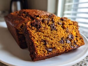 Close-up of moist pumpkin bread with visible chocolate chips, sliced and resting on a white plate.