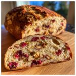 A thick slice of moist cranberry walnut bread showing visible cranberries and walnuts in the airy crumb.