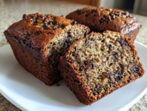 Close-up of three moist mini banana bread loaves, one sliced to show chocolate chips inside.