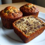 Close-up of three moist mini banana bread loaves, one sliced to show chocolate chips throughout the crumb.