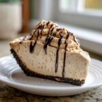 A decadent slice of no bake peanut butter pie with a thick chocolate crust, topped with whipped peanut butter filling and chocolate syrup drizzle.