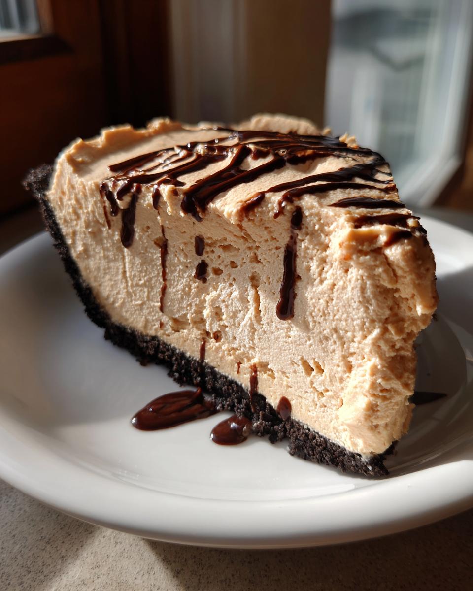 A close-up slice of fluffy no bake peanut butter pie with a dark chocolate crust and drizzled with chocolate sauce.