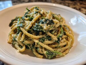 Close-up of creamy spinach pasta served on a white plate, featuring thick noodles coated in sauce and wilted spinach.