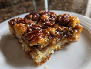 Close-up of a square slice of pecan pie cobbler recipe showing a gooey, caramelized pecan topping over a soft base.