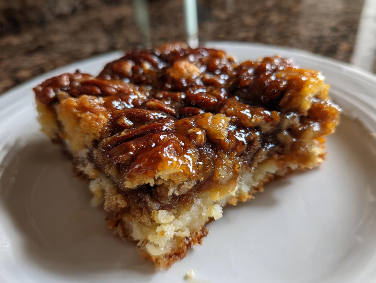 Close-up of a square slice of pecan pie cobbler recipe showing a gooey, caramelized pecan topping over a soft base.