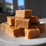 A stack of rich, square-cut pieces of homemade penuche fudge resting on a white plate.