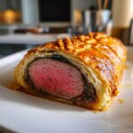 Cross-section of a perfectly cooked beef wellington recipe showing medium-rare pink tenderloin inside golden puff pastry.