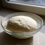 A large, risen ball of pizza dough recipe resting in a clear glass bowl, ready for the next step.