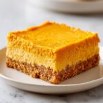 A close-up of one square pumpkin cheesecake bars slice showing a thick, bright orange topping over a graham cracker crust.