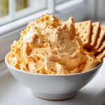 A bowl filled with light, airy orange pumpkin fluff dip served alongside square crackers.