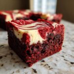 A single, rich square of red velvet cheesecake brownies showing a deep red base and a creamy white cheesecake swirl top.