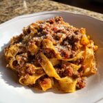 Close-up of rich bolognese sauce generously coating wide pappardelle pasta, topped with grated Parmesan cheese.