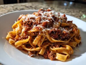 Close-up of fresh tagliatelle pasta generously topped with rich bolognese sauce and grated Parmesan cheese.