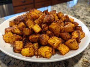 A mound of golden brown, roasted Mexican potatoes seasoned with spices, served on a white plate.