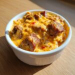 Close-up of a warm, cheesy serving of sausage rotel dip topped with browned sausage chunks in a white ramekin.