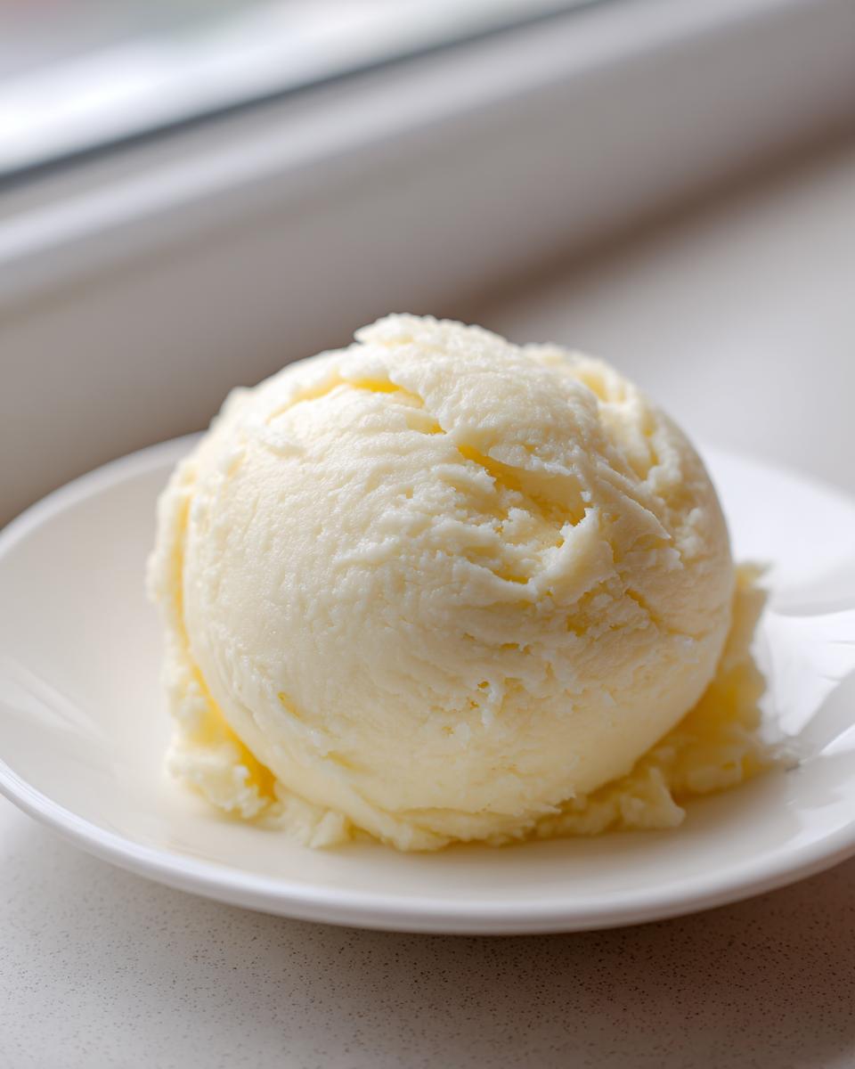 A single, smooth, perfectly scooped ball of pale yellow fufu resting on a small white plate.