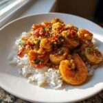 A close-up of flavorful shrimp etouffee served generously over white rice on a white plate.
