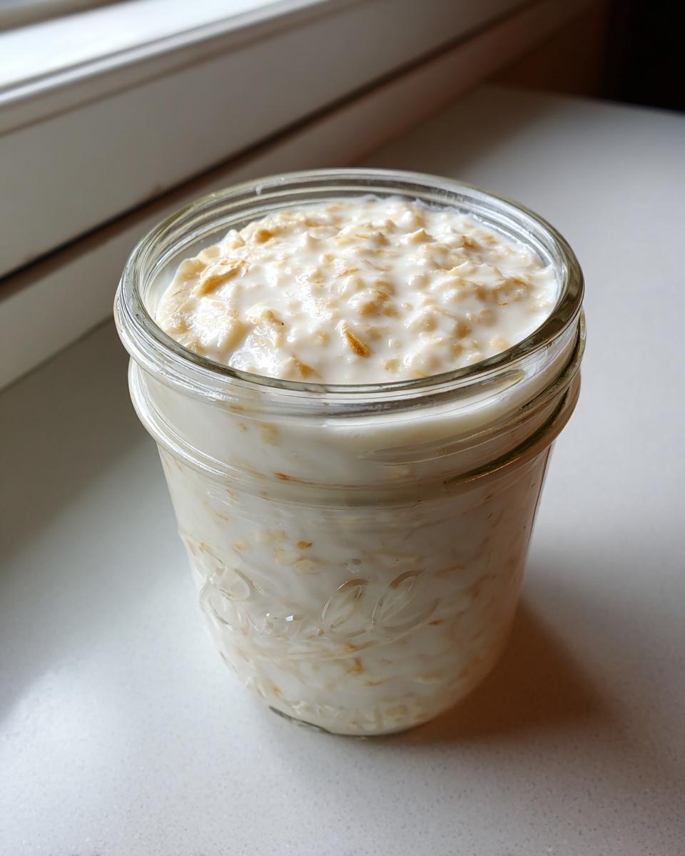 Close-up of basic overnight oats soaking in milk inside a clear glass mason jar.