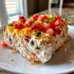 A thick, creamy slice of 5-ingredient boat dip topped with shredded cheese, diced tomatoes, and green peppers.
