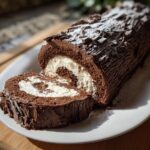 A cross-section view of a rich chocolate yule log cake filled with white cream and dusted with powdered sugar.