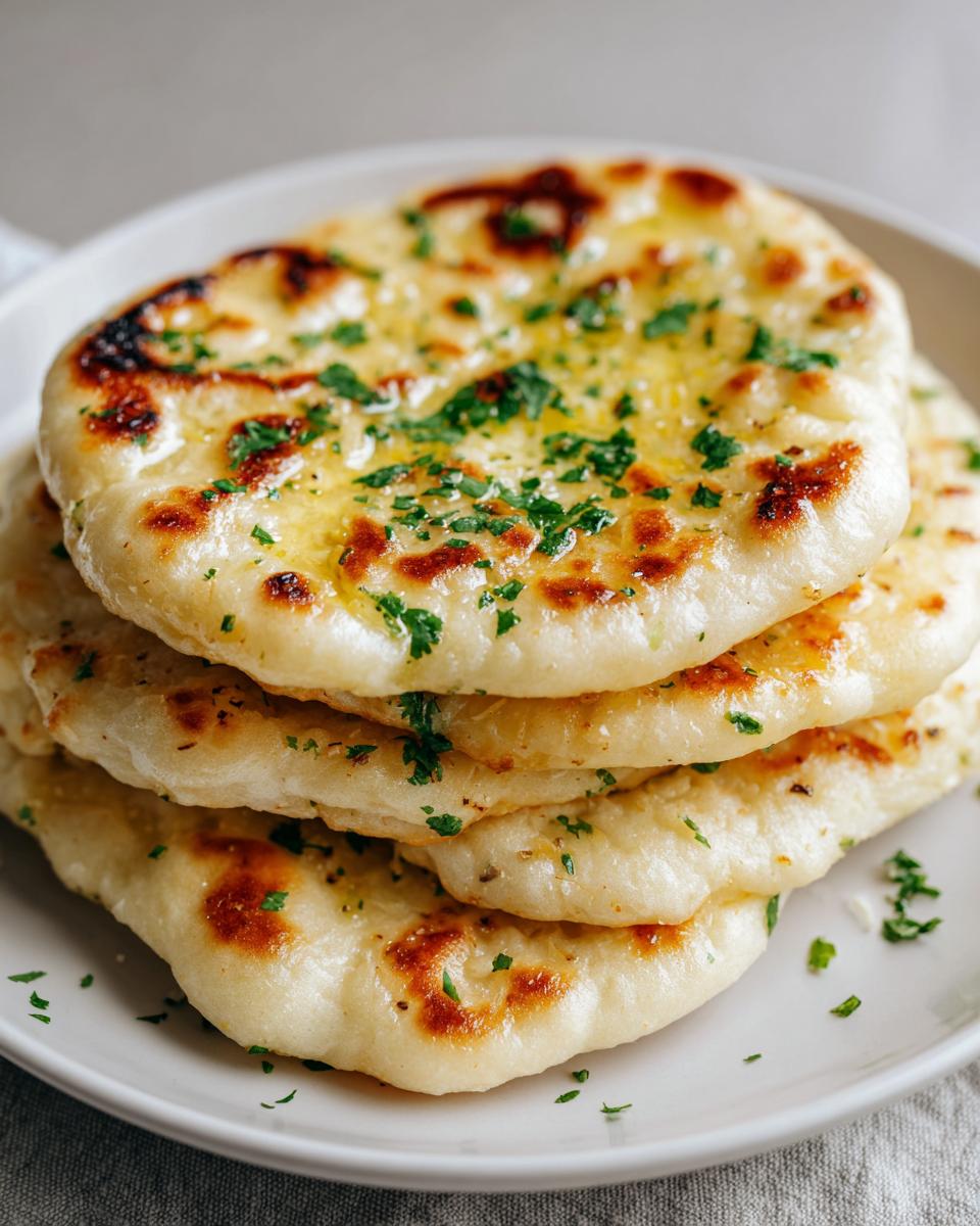 A stack of four fluffy, homemade naan bread pieces brushed with butter and topped with fresh chopped parsley.