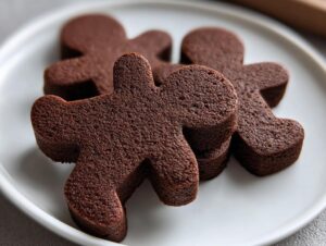 Close-up of several thick, dark brown soft gingerbread cookies shaped like gingerbread men stacked on a white plate.