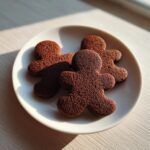 Close-up of three freshly baked, dark brown soft gingerbread cookies shaped like people on a white plate.