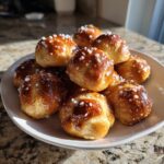 A pile of freshly baked, glossy soft pretzel bites sprinkled with coarse salt, served on a white plate.
