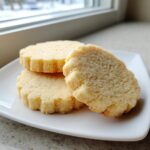Close-up of three soft, thick sugar cookies sprinkled with coarse sugar, resting on a white square plate.