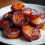 Close-up of thick-cut, caramelized Southern candied yams piled high on a white plate.