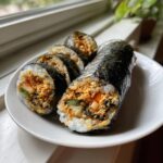 Close-up of sliced spicy tuna kimbap rolls filled with seasoned tuna, rice, and vegetables, served on a white plate.