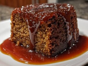 A close-up, decadent shot of a single serving of sticky toffee pudding recipe covered in glossy toffee sauce.