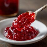 A spoonful of vibrant, chunky strawberry freezer jam being lifted from a small white dish.