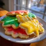 A stack of tree-shaped sugar cookies topped with glossy, hardened red, green, and yellow cookie icing.