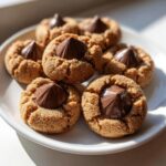 A plate of freshly baked peanut butter blossoms, featuring crinkled peanut butter cookies topped with melted chocolate kisses.