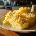 A generous serving of fluffy, yellow creamy mashed potatoes with peaks and valleys on a white plate.