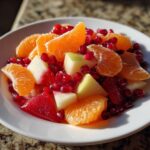 Close-up of a vibrant winter fruit salad featuring bright orange segments, white apple chunks, and deep red pomegranate seeds.