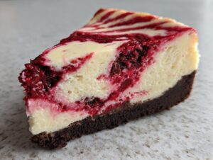 A close-up slice of white chocolate raspberry cheesecake featuring a rich, dark crust and vibrant raspberry swirls.