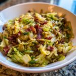 Close-up of a delicious 15-minute cabbage recipe featuring sautéed cabbage topped with crispy bacon pieces in a white bowl.